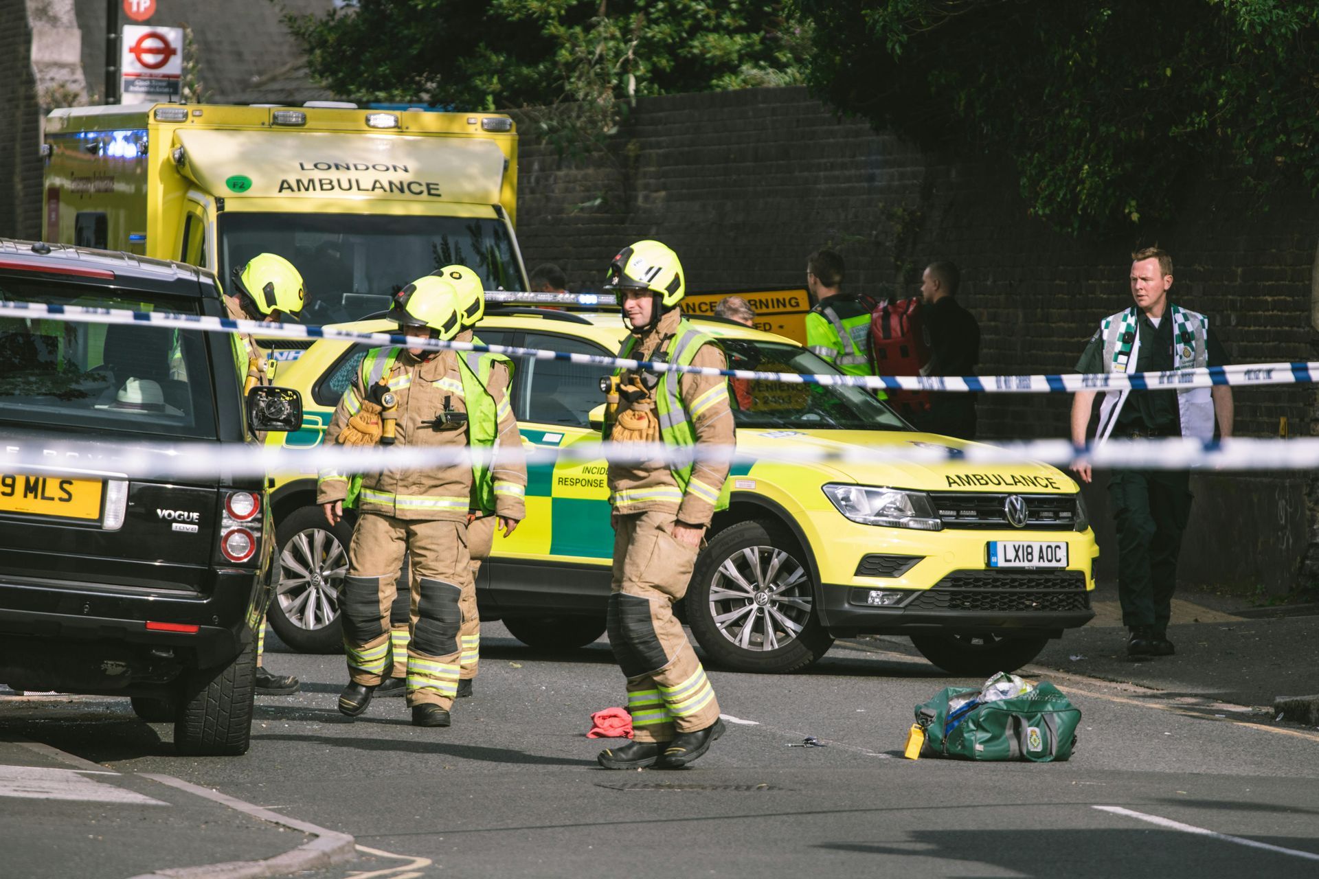 Firefighters and paramedics at a street scene with emergency vehicles. Yellow and blue, cordon tape.