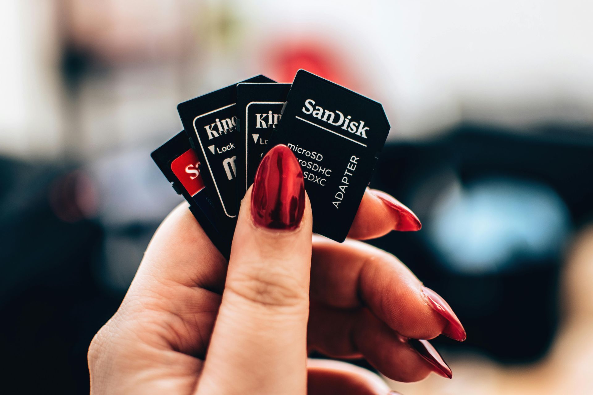 Hand holding three SD cards with red nail polish.