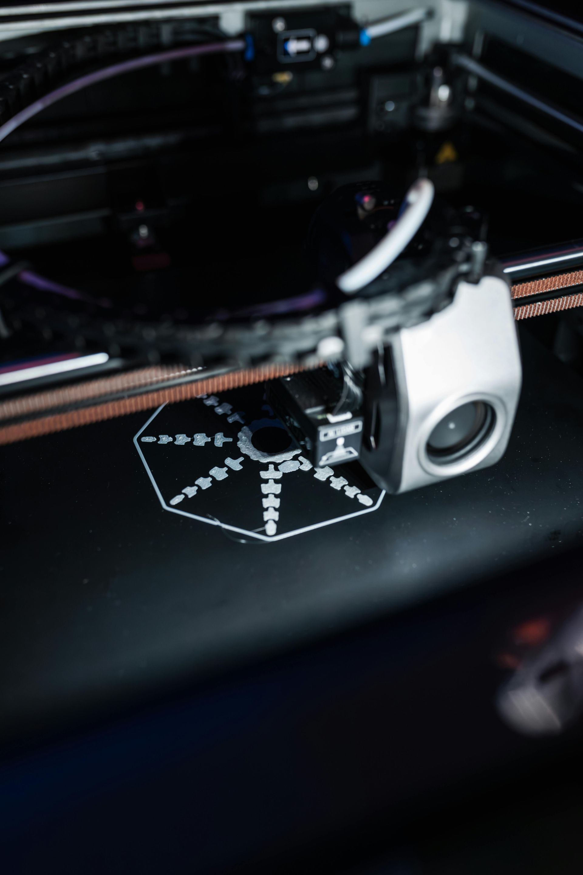 3D printer in action, printing a white, hexagonal test pattern on a black surface.