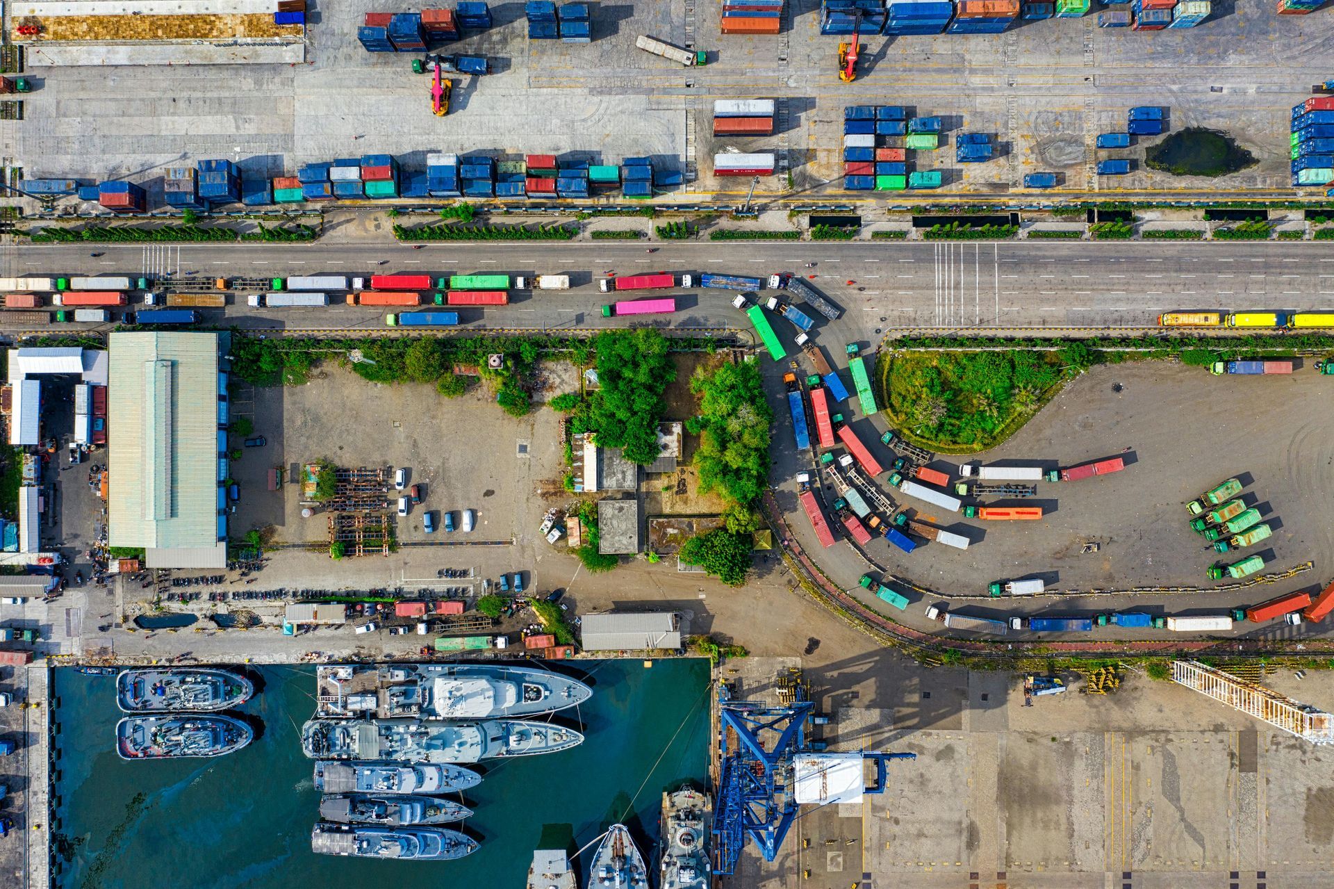 Aerial view of a busy port with ships docked, containers, trucks, and loading operations.