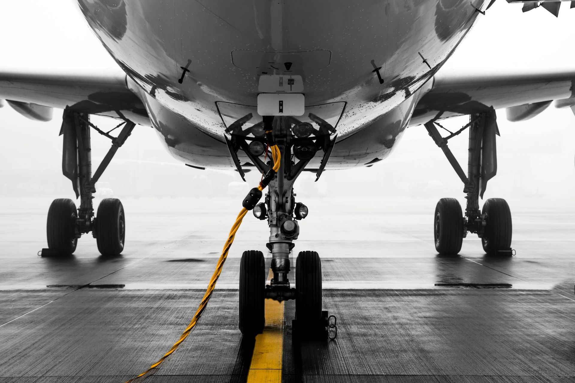 Airplane front view, black and white with yellow power cord, on wet tarmac.