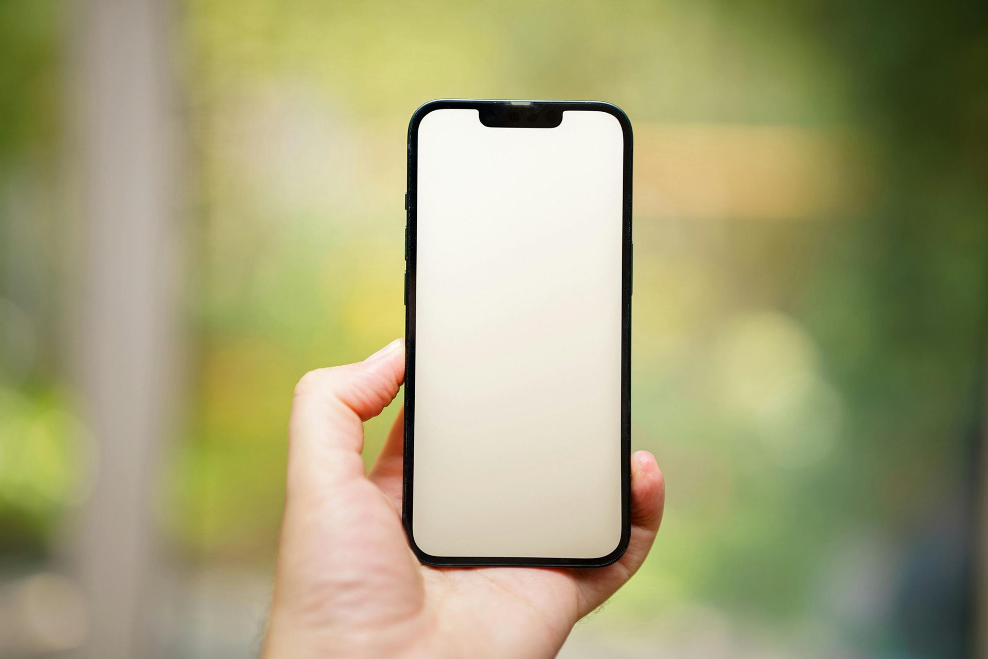 Hand holding a smartphone with a blank screen against a blurred green background.