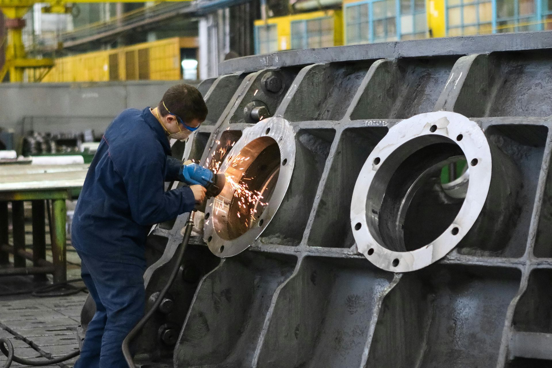 Man in blue coveralls grinding metal inside a large industrial machine in a factory.