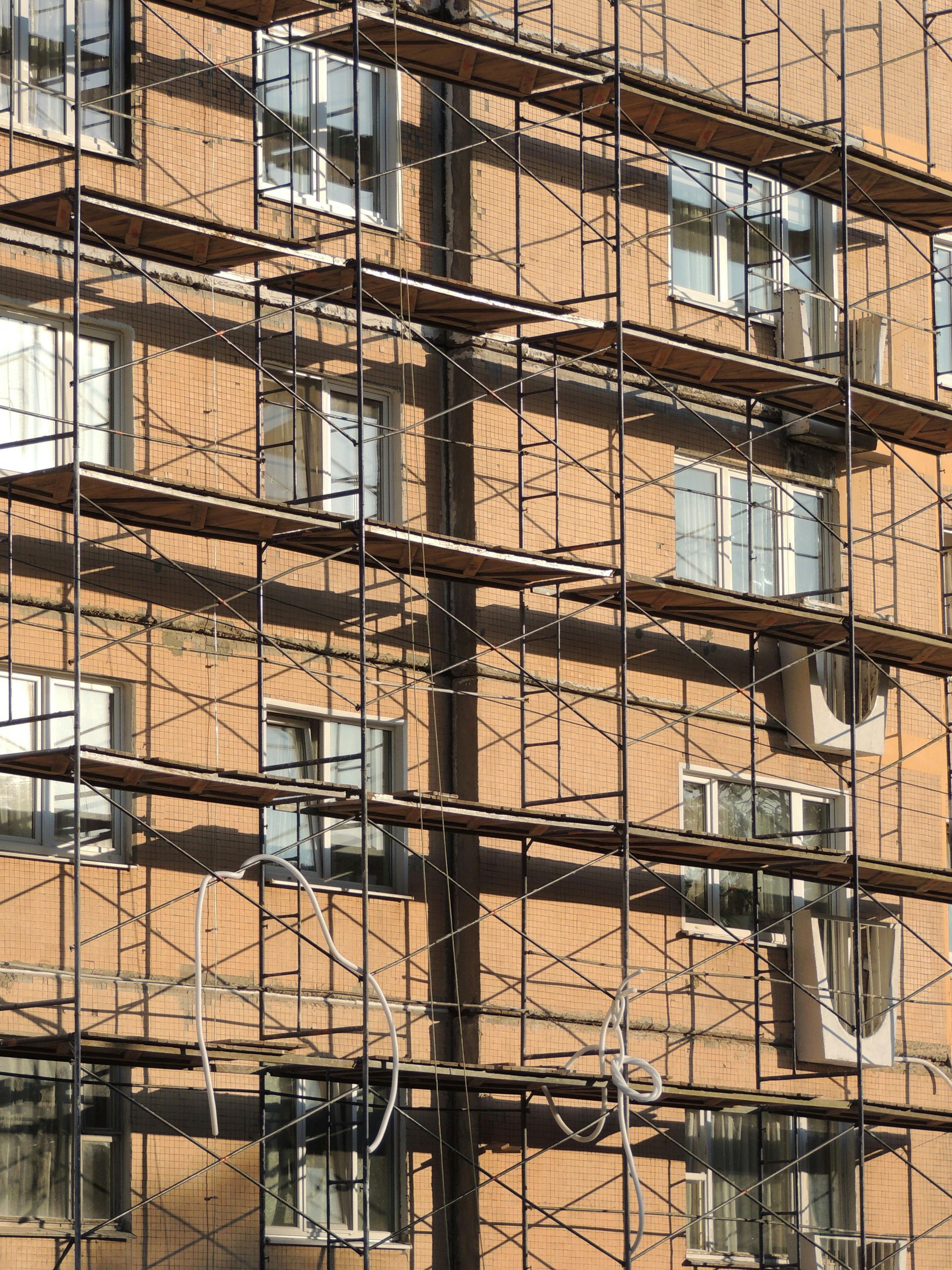 Scaffolding on the side of a building with windows. The building is brown.