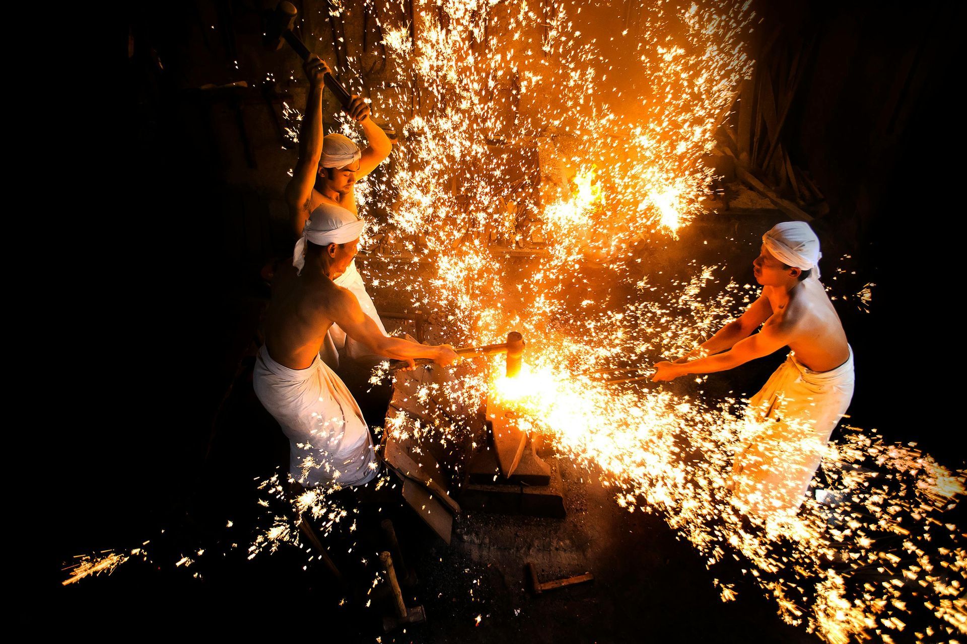 Blacksmiths forging metal with sparks flying.