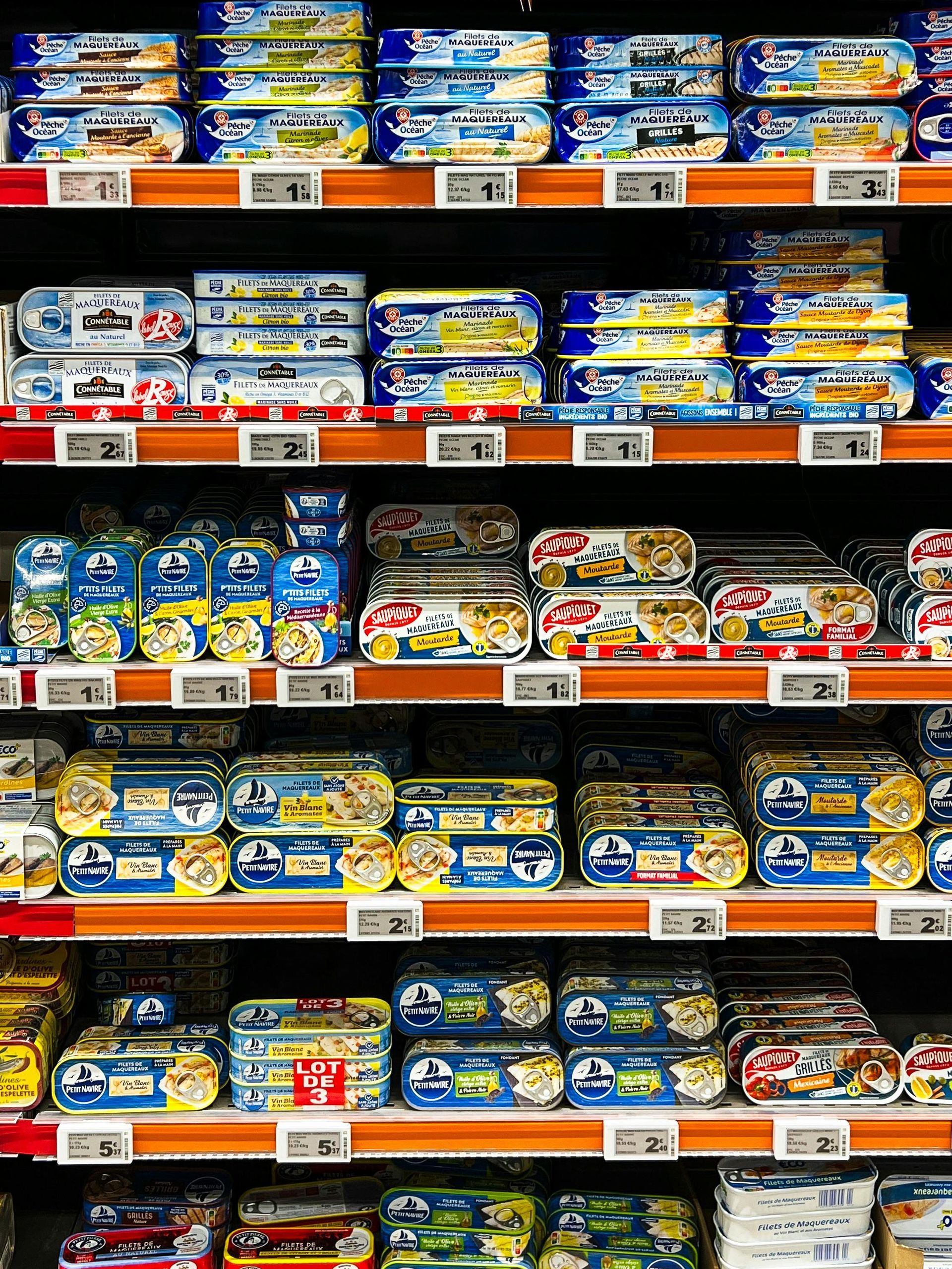 Shelves stocked with various canned goods, mostly seafood, in a brightly lit grocery store.