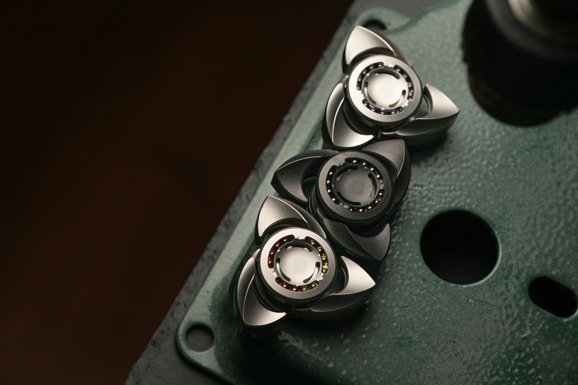Three silver and black fidget spinners on a green surface.