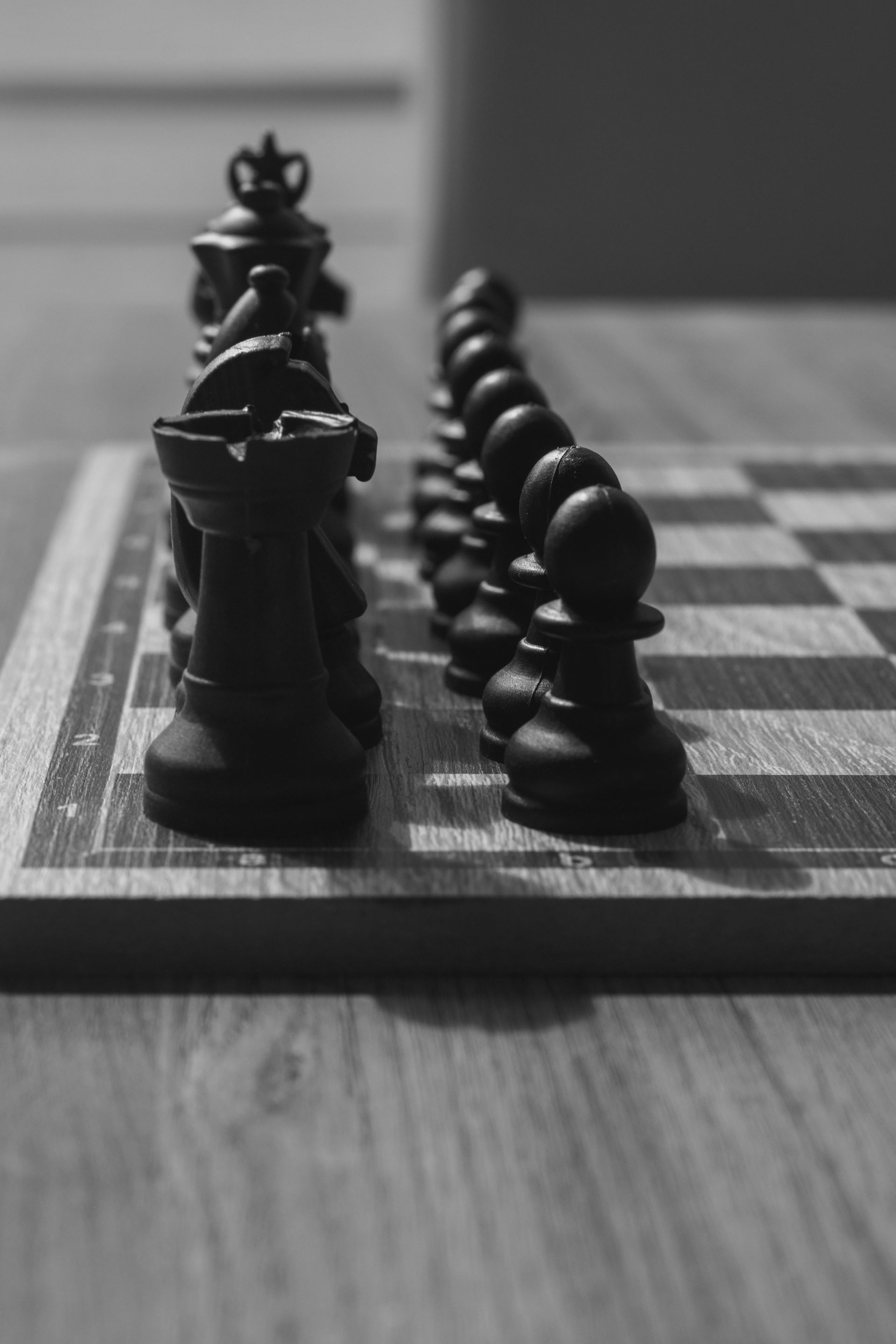 Black chess pieces lined up on a wooden board, ready to play.