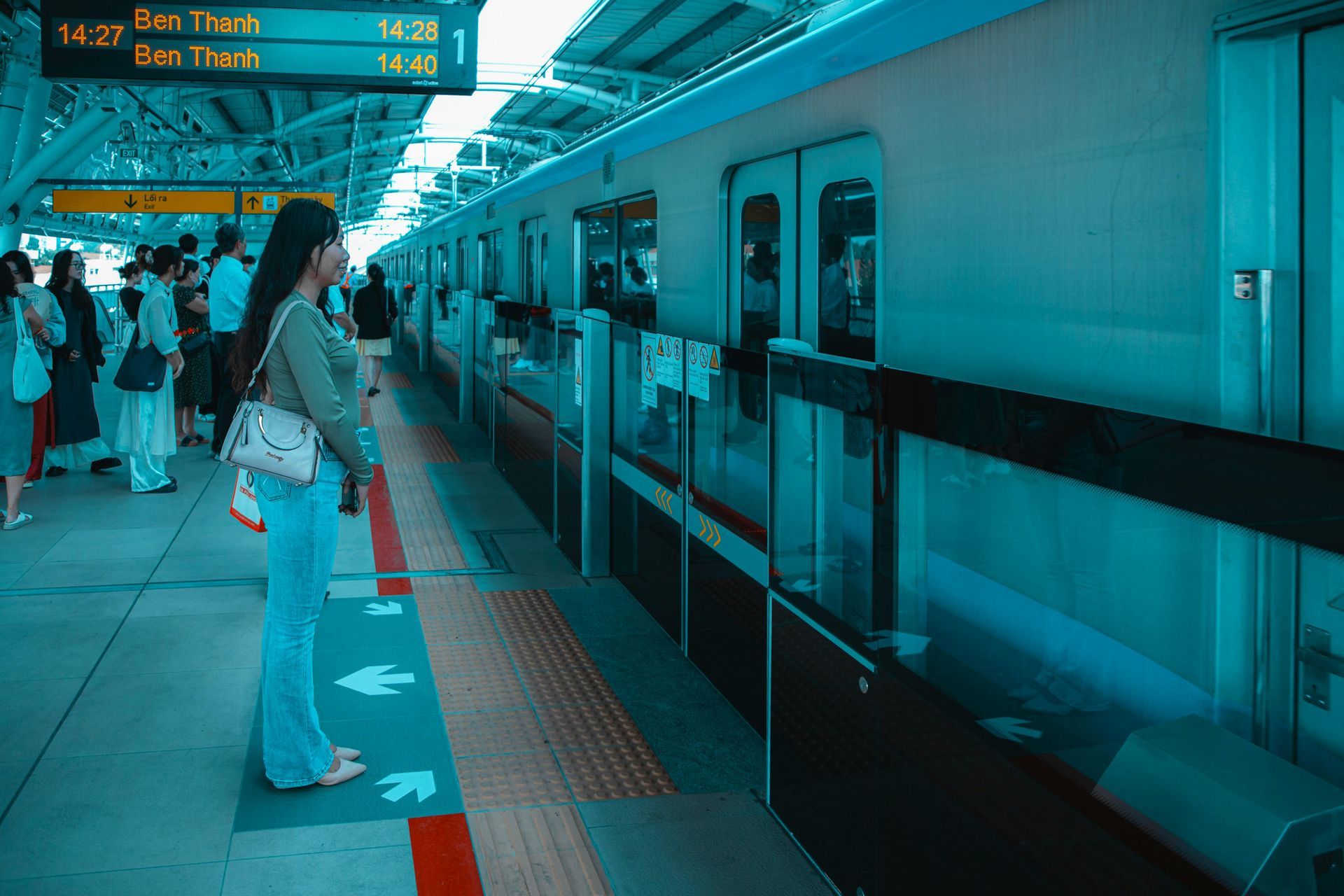 Woman at a train station waiting for the train. People stand by the platform. The train is in view.