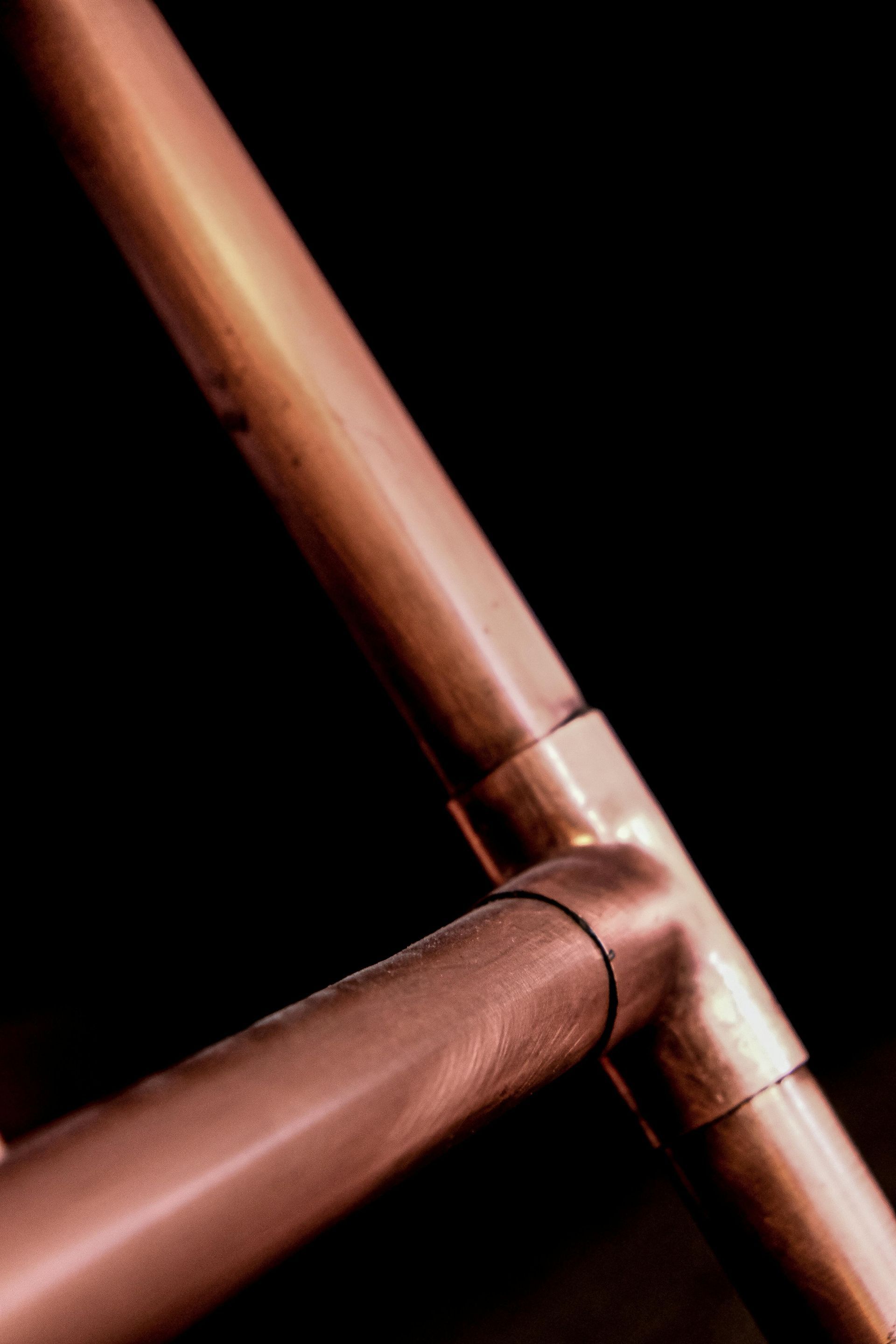 Copper pipes connected by a T-joint, angled against a dark background.