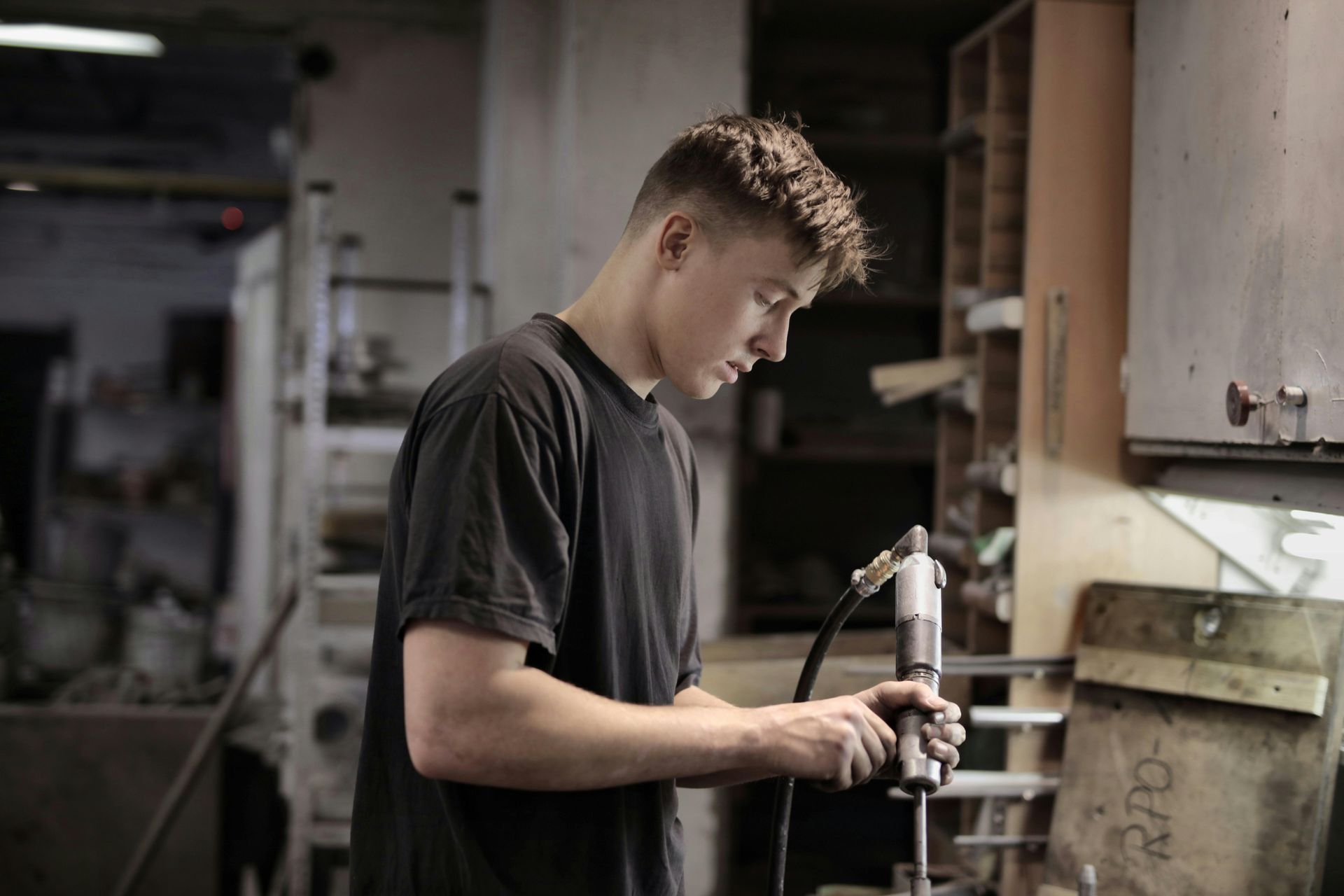 Young man in black shirt working with a tool in a workshop.