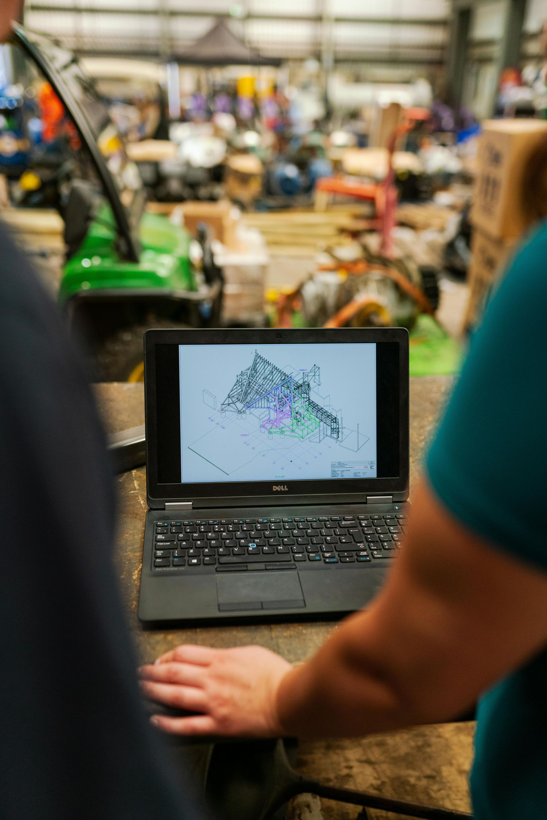 Two people looking at a laptop screen displaying a colorful data map in a cluttered warehouse.