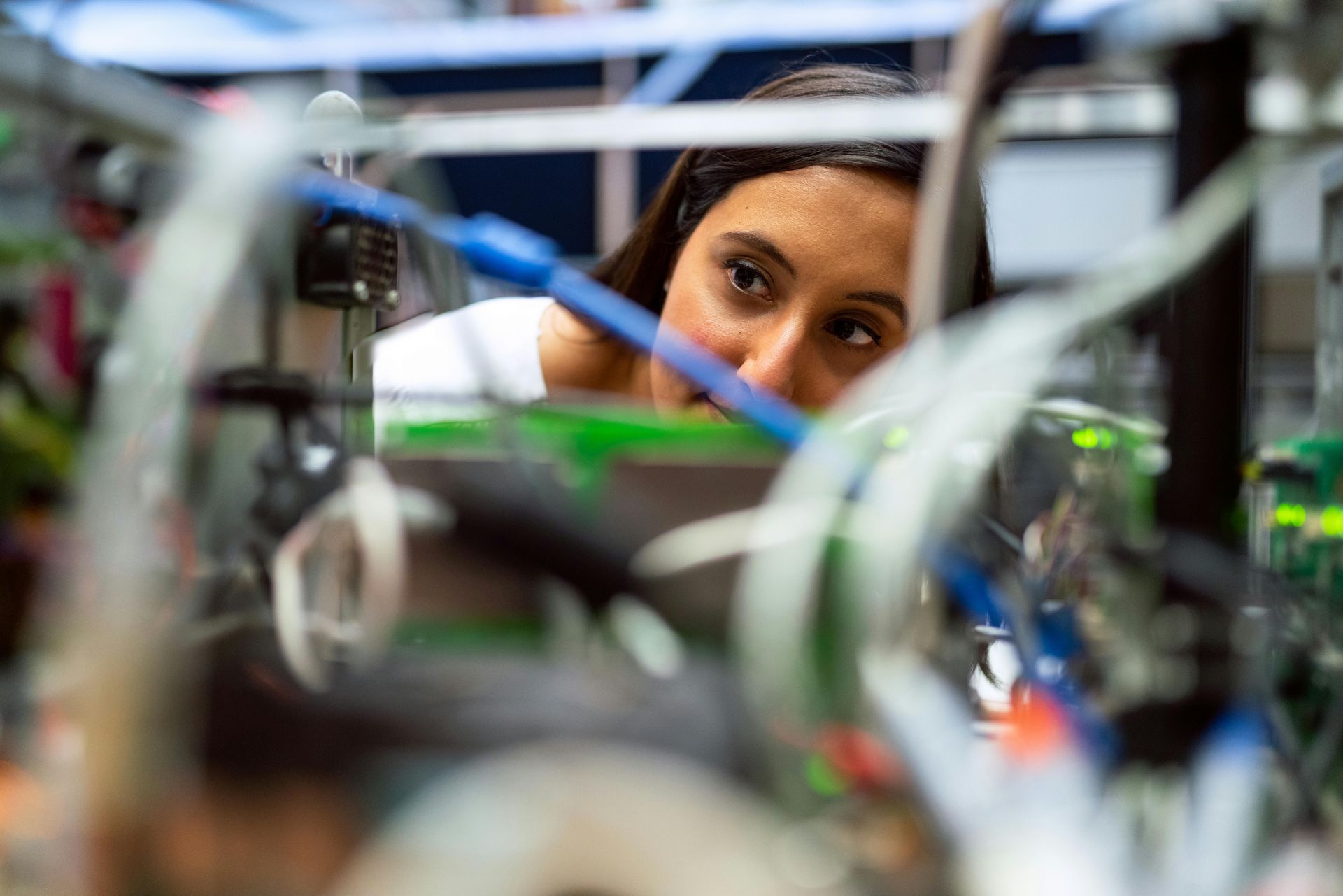 Woman intently examines complex machinery with blue and white wires in a lab.