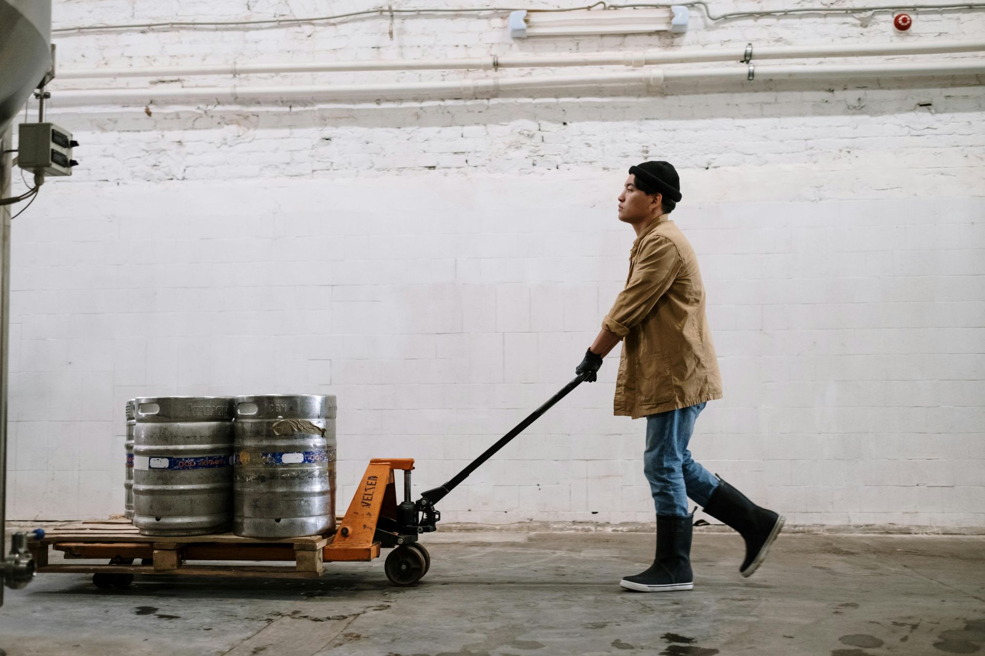 Man in a warehouse pulls a pallet with beer kegs.