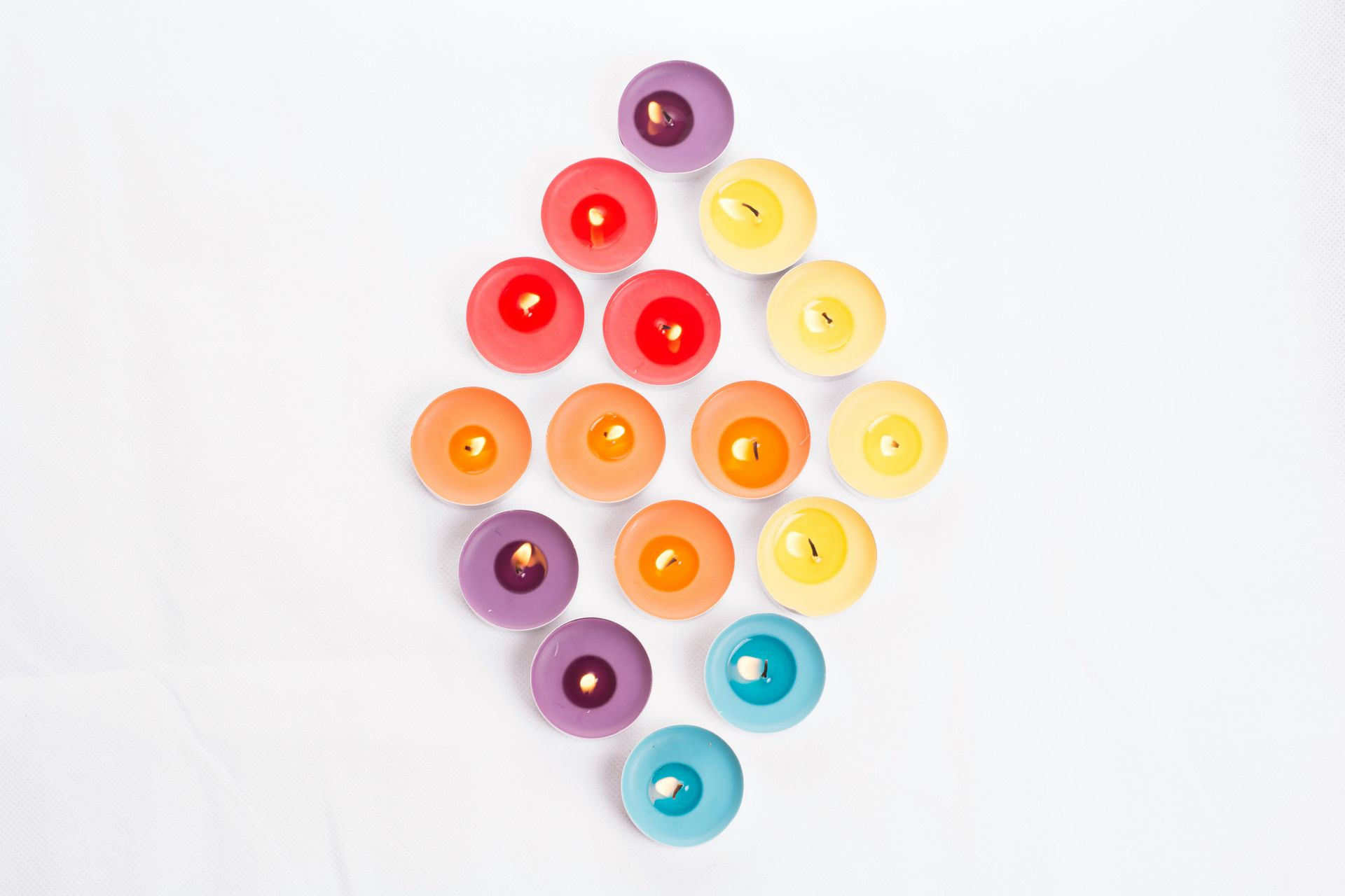 Colorful candles arranged in a diamond shape on a white surface.