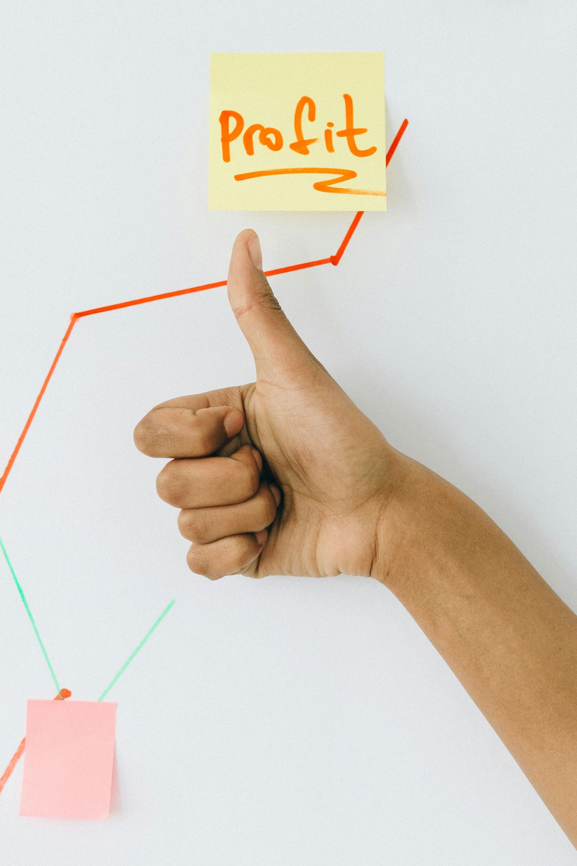 Hand with thumbs-up gesture next to a rising red profit graph and yellow sticky note.