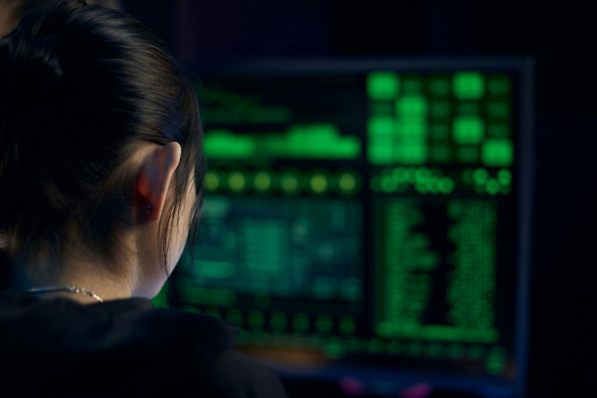 Woman with dark hair looking at a computer screen with green code; dim setting.