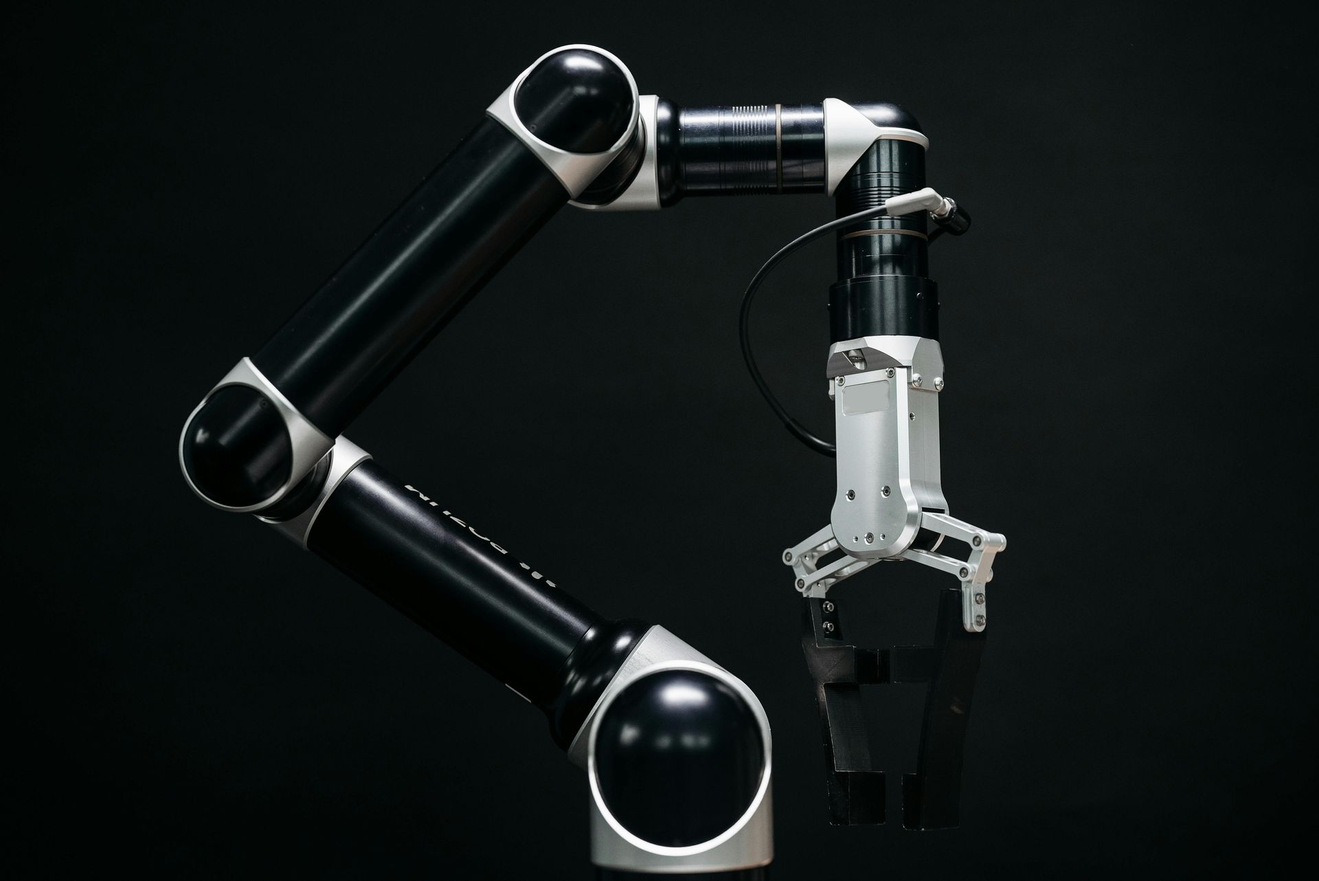 Black and silver robotic arm with gripper against a dark background.