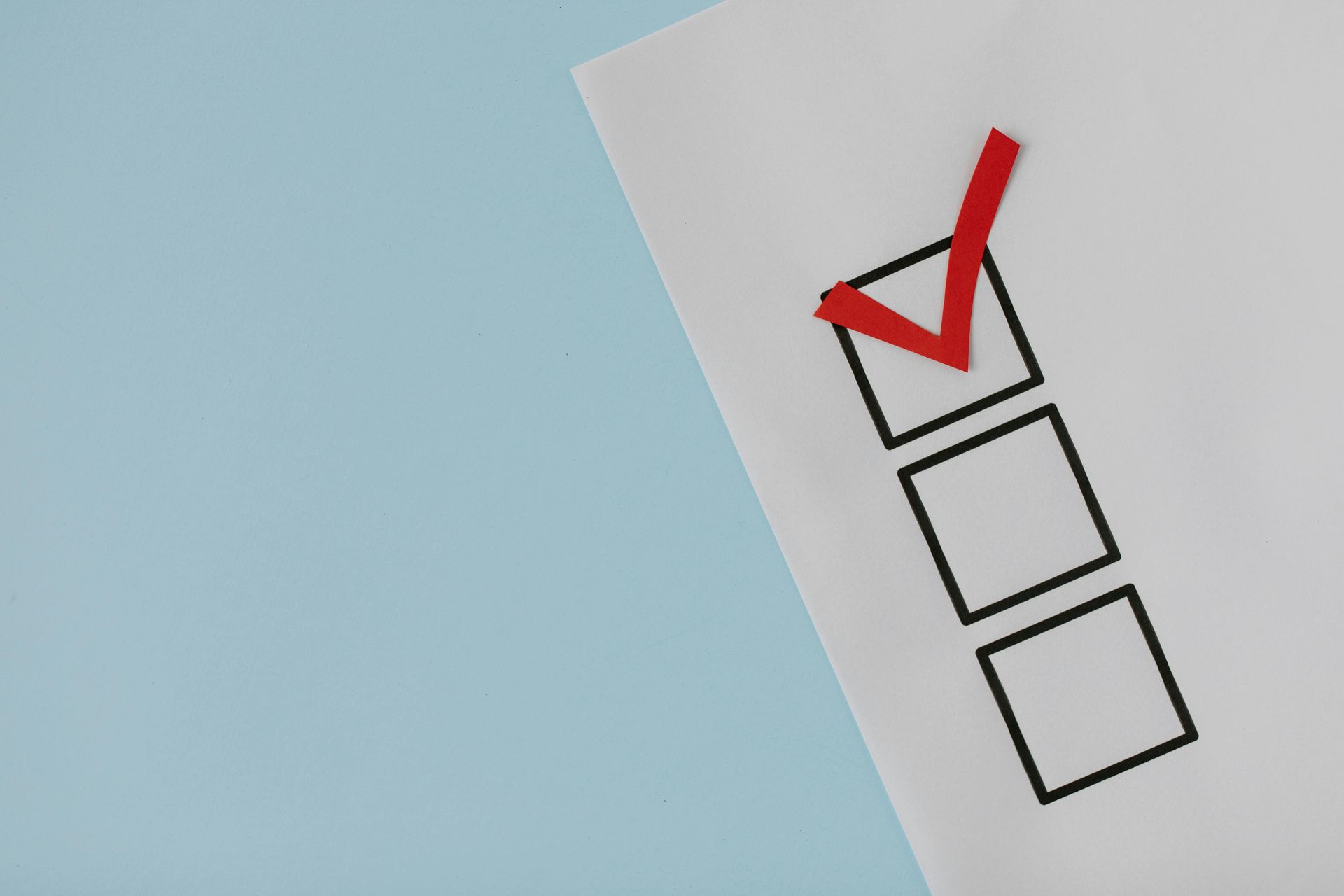 Checkmark in red, marking a box on a white paper with blank boxes, on a light blue background.