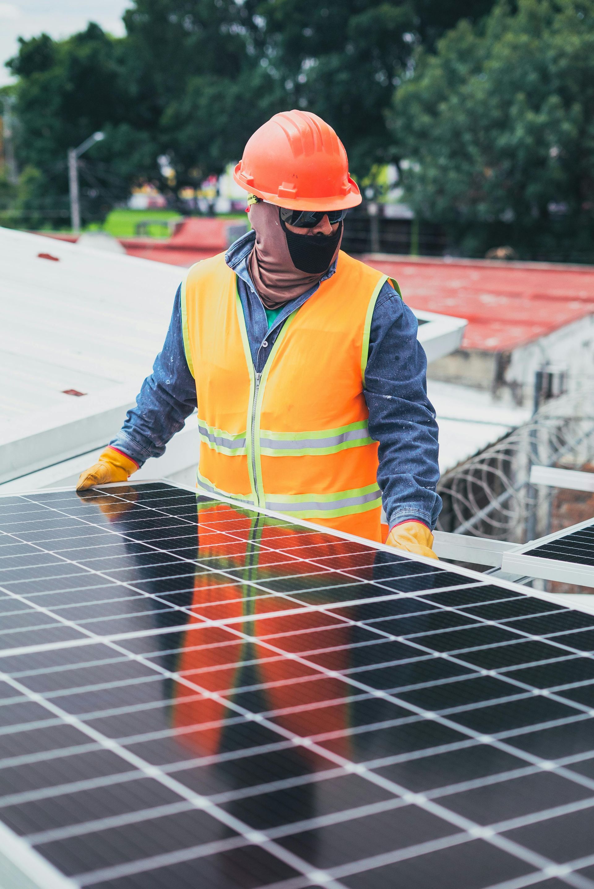 Construction worker in orange vest and hardhat installing solar panels on a rooftop.
