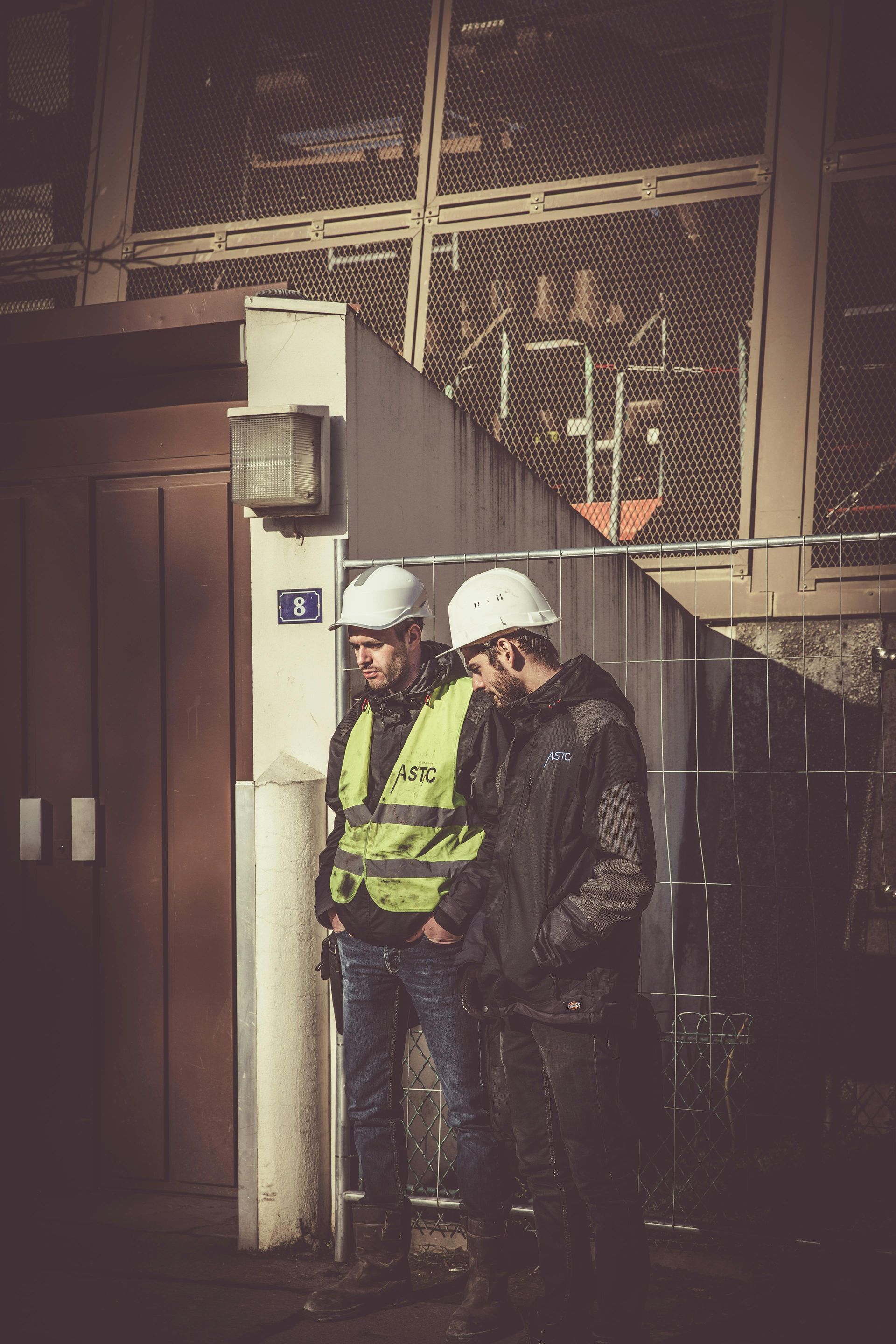 Two construction workers in hard hats and reflective vests; discussing plans near a building interior.