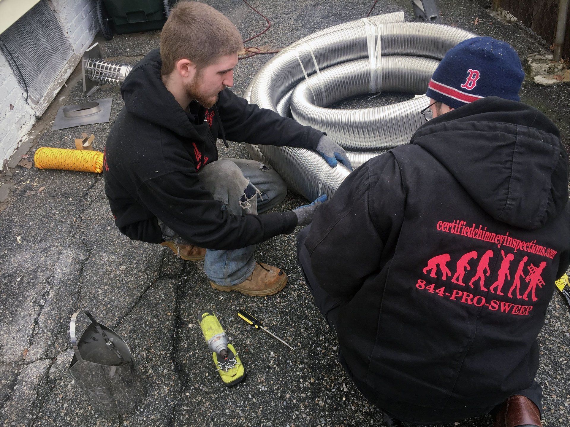 A man wearing a black jacket with a red logo on the back is working on a pipe
