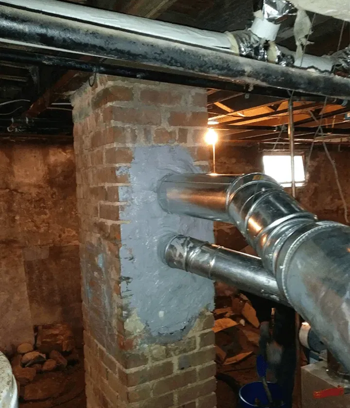 A brick chimney with metal pipes attached to it in a basement.
