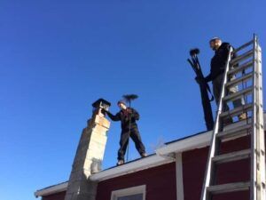 Two men are working on a chimney on the roof of a house.
