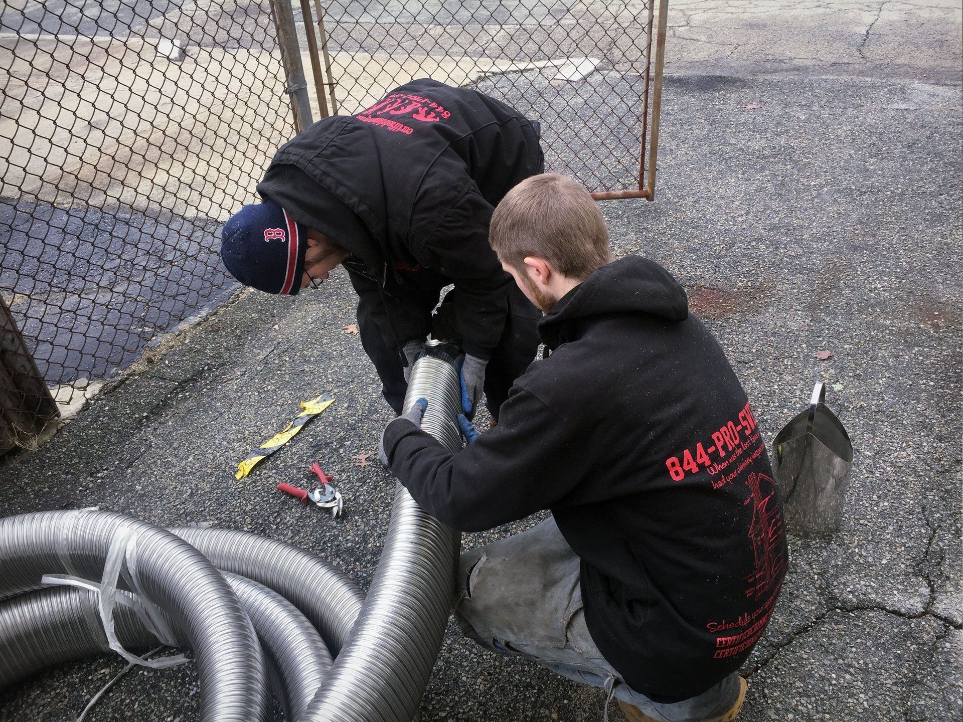 Two men are working on a hose with a fence in the background