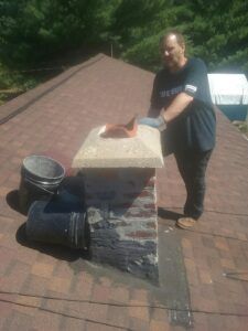 A man is standing on top of a roof next to a chimney.