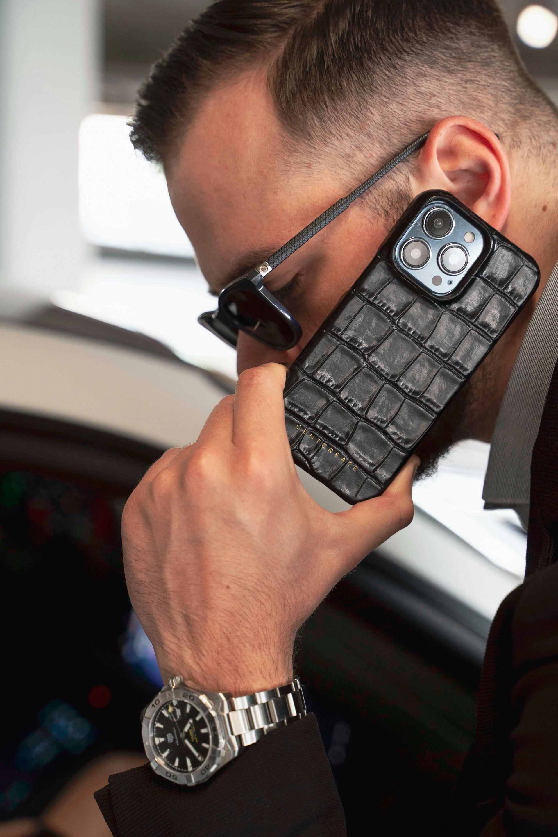 A person in a suit wears a metal watch and talks on a phone with a textured, crocodile-patterned case.