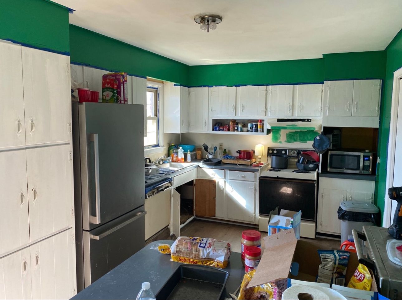 Kitchen with white cabinets, green walls, stainless steel refrigerator, and cooking appliances.