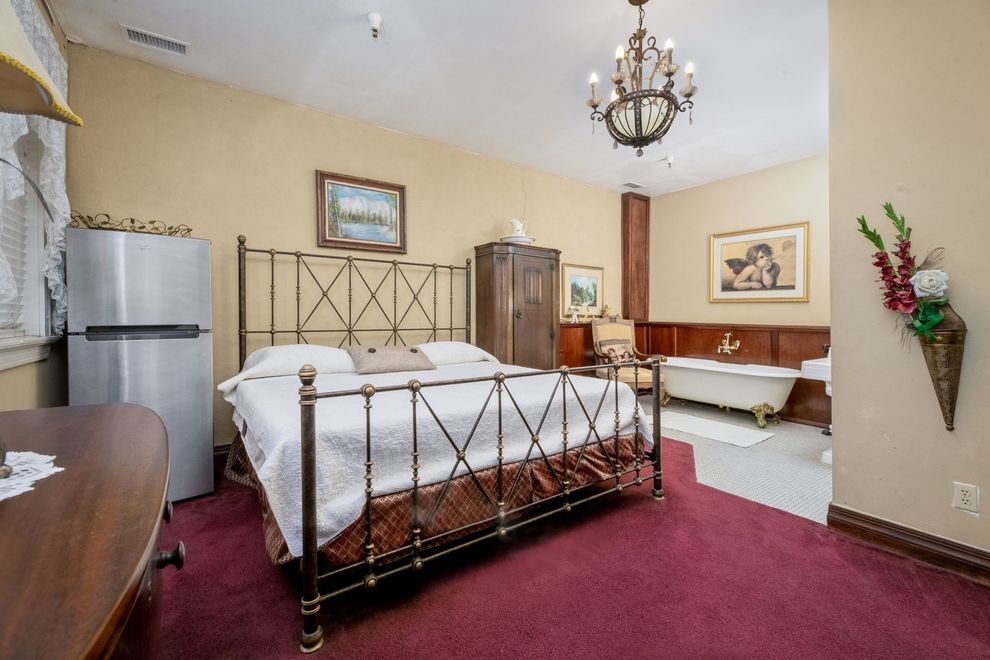 A bedroom with a king size bed , a refrigerator , and a bathtub.