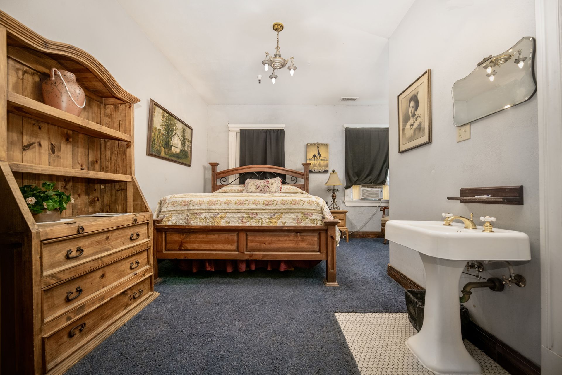 A bedroom with a bed , dresser , sink and mirror.