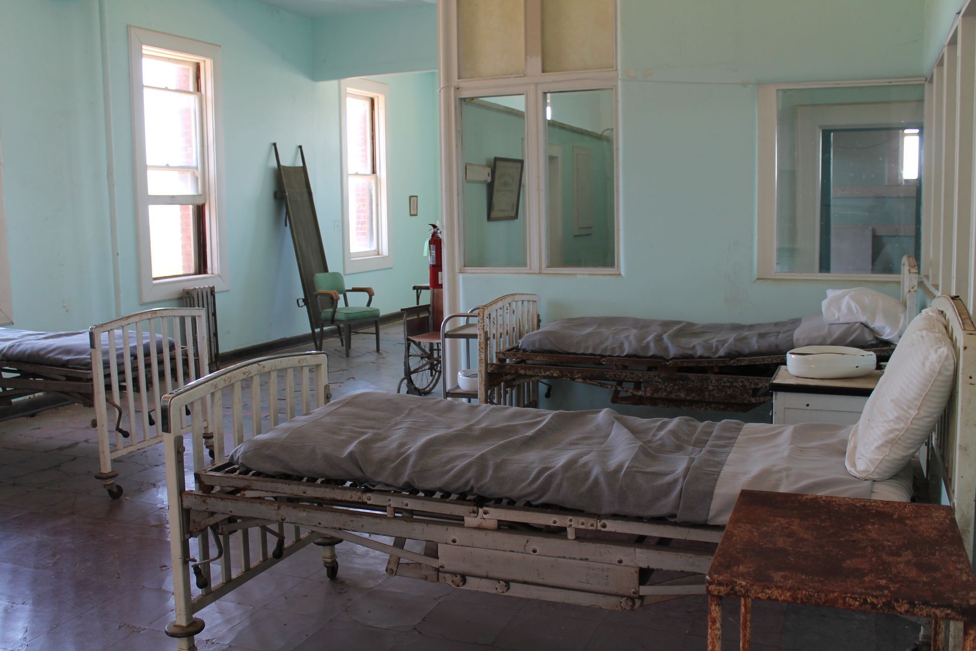 A hospital room with a lot of beds and a fire extinguisher.