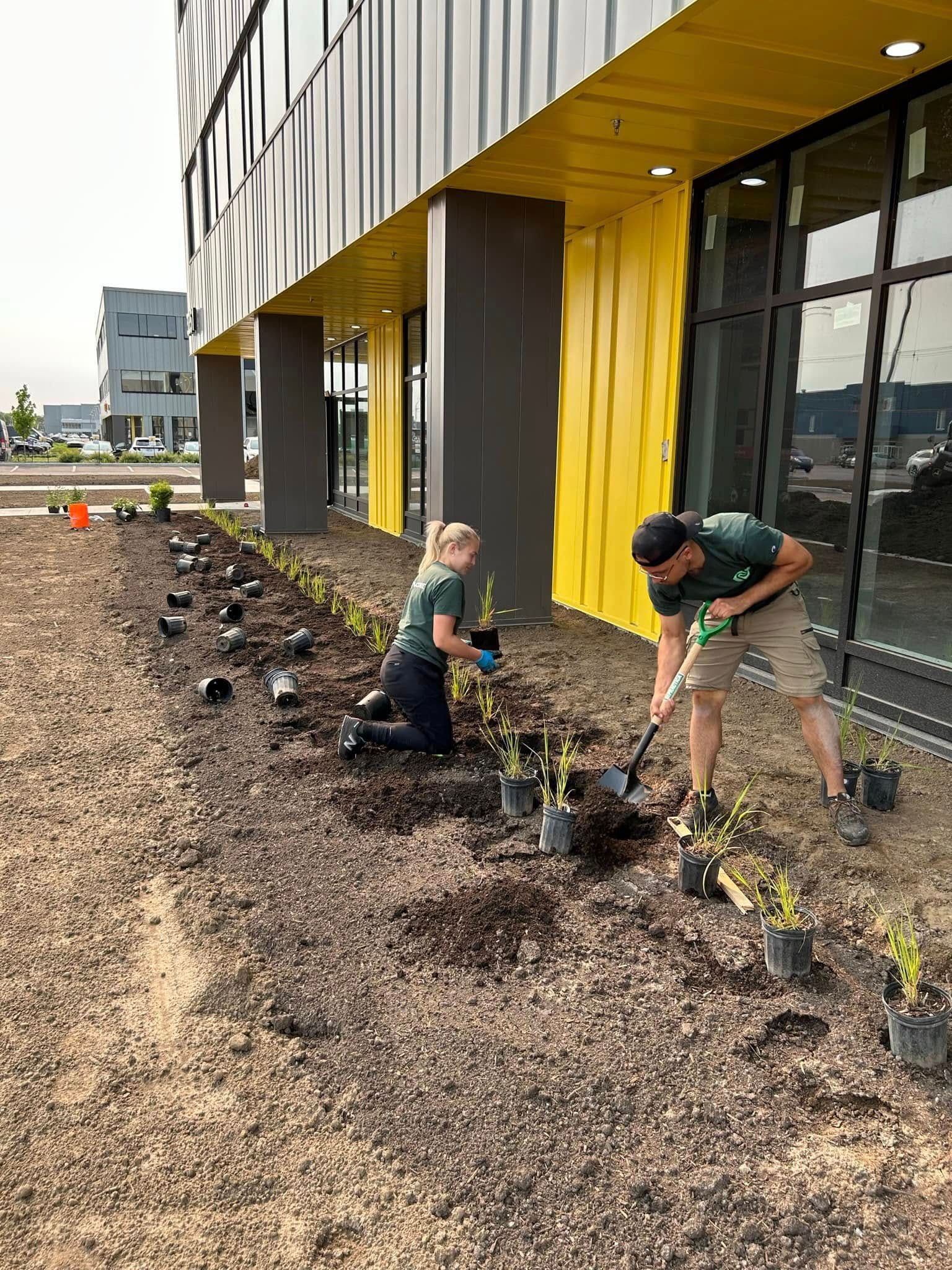 Un homme et une femme plantent des plantes dans un jardin devant un bâtiment.