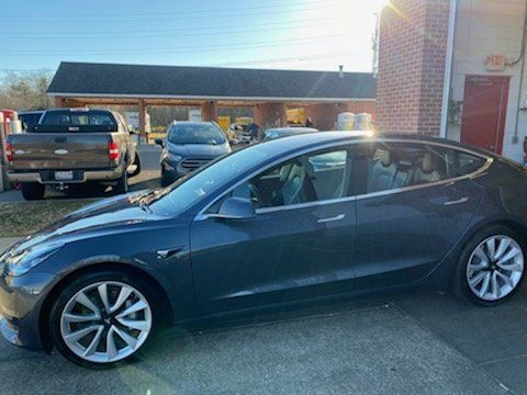 A tesla model 3 is parked in front of a building.