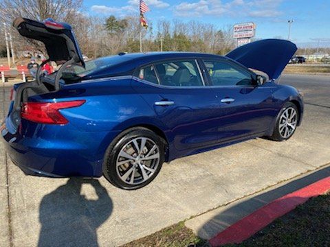 A blue nissan maxima with its trunk open is parked in a parking lot.
