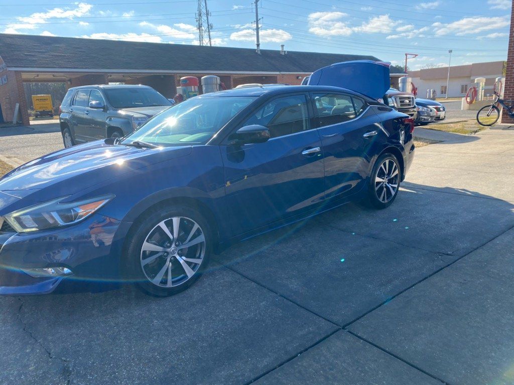 A blue car with the hood up is parked in a parking lot.