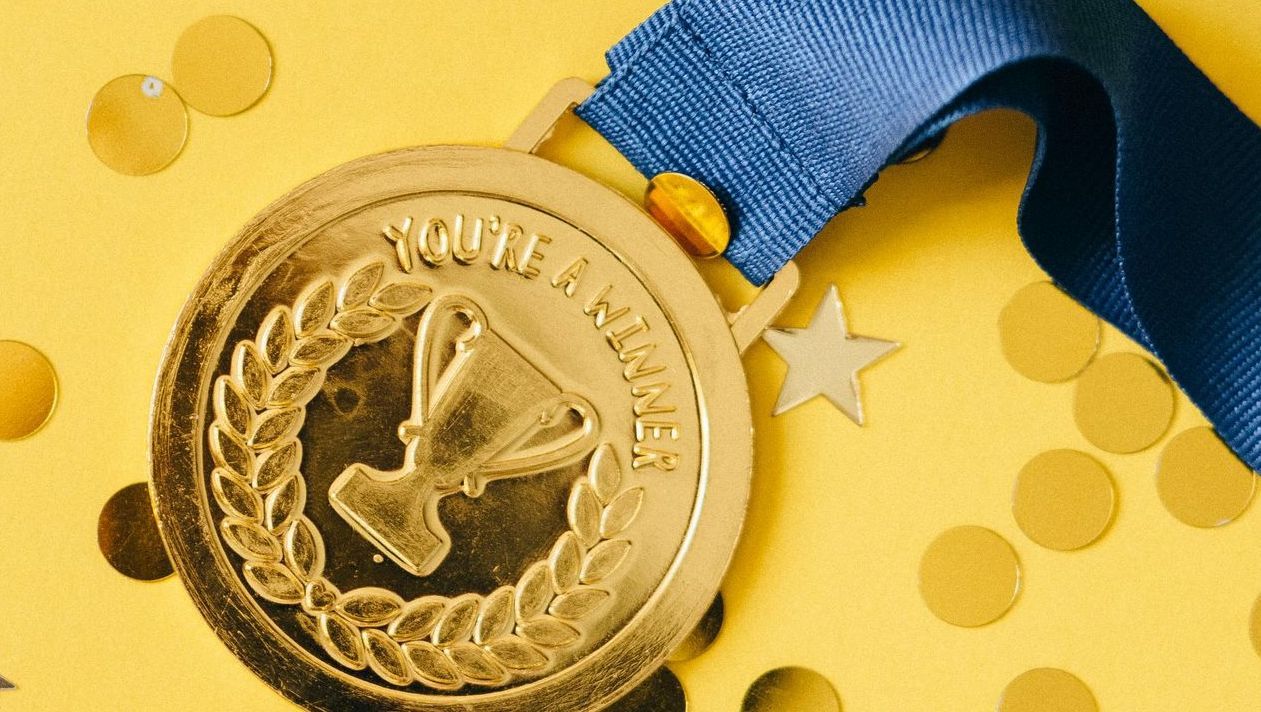 A gold medal with a blue ribbon on a yellow background.
