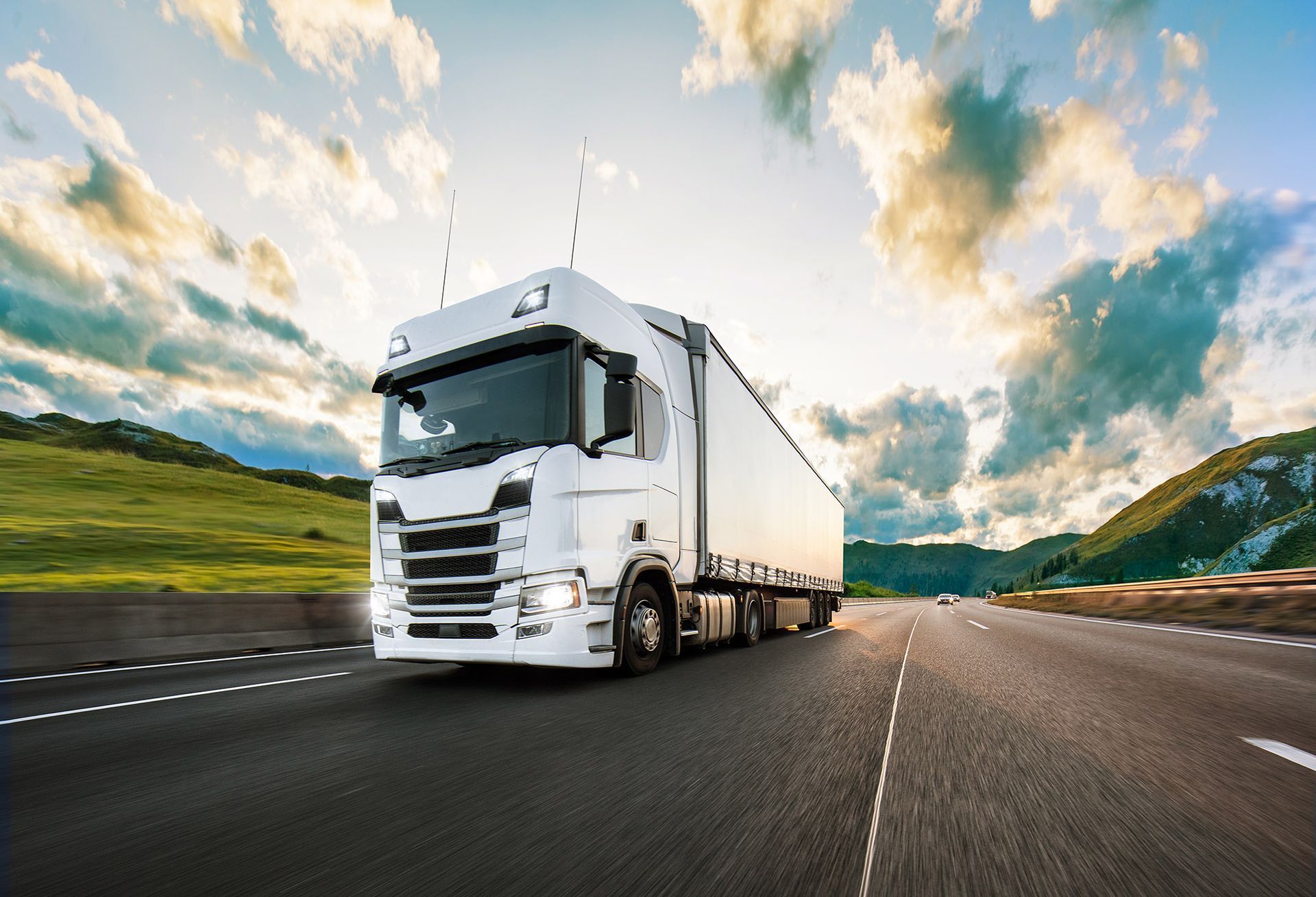 White semi-truck driving on a highway, under a cloudy sky.