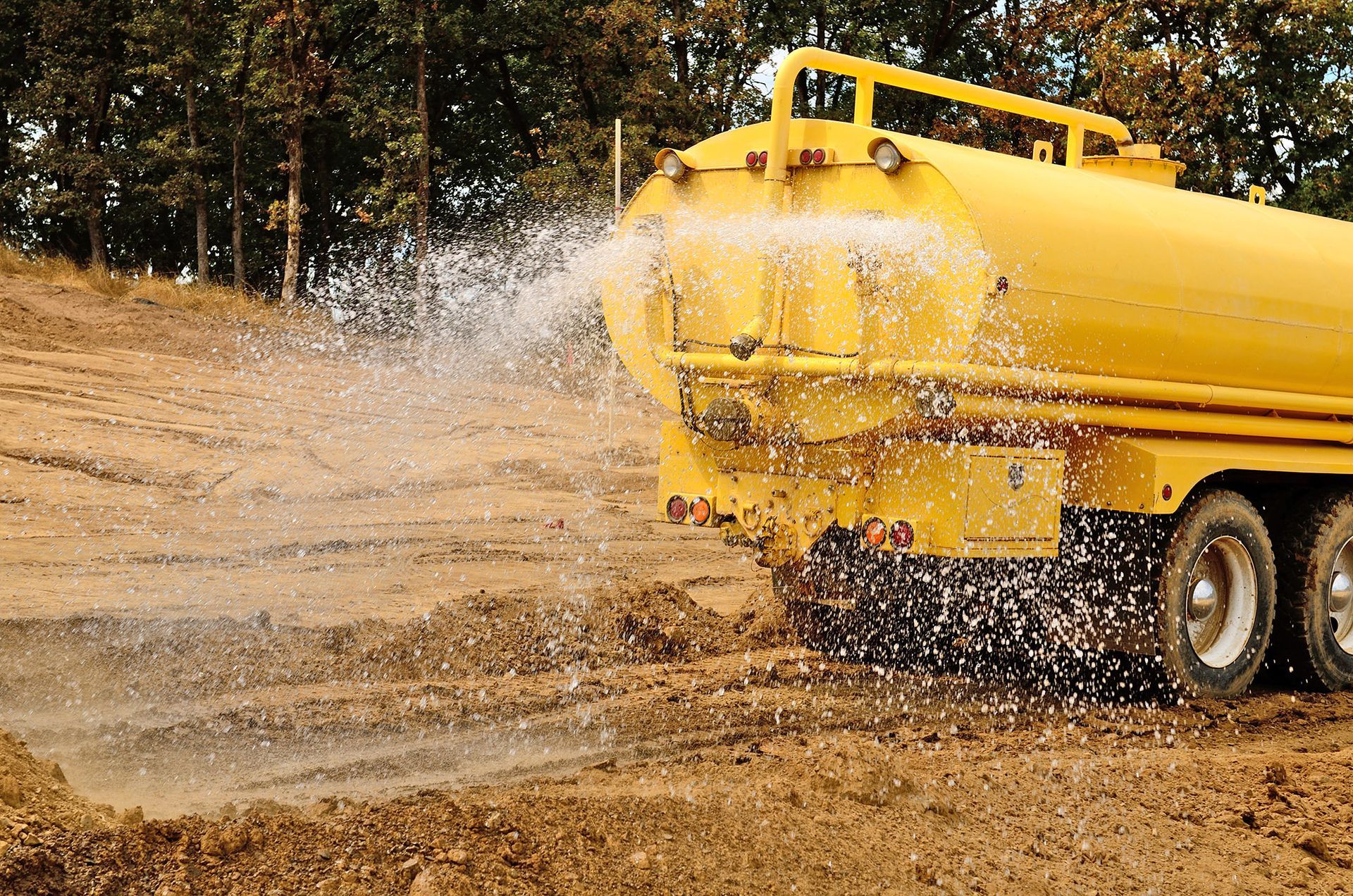 Yellow water truck spraying water onto a dirt road.