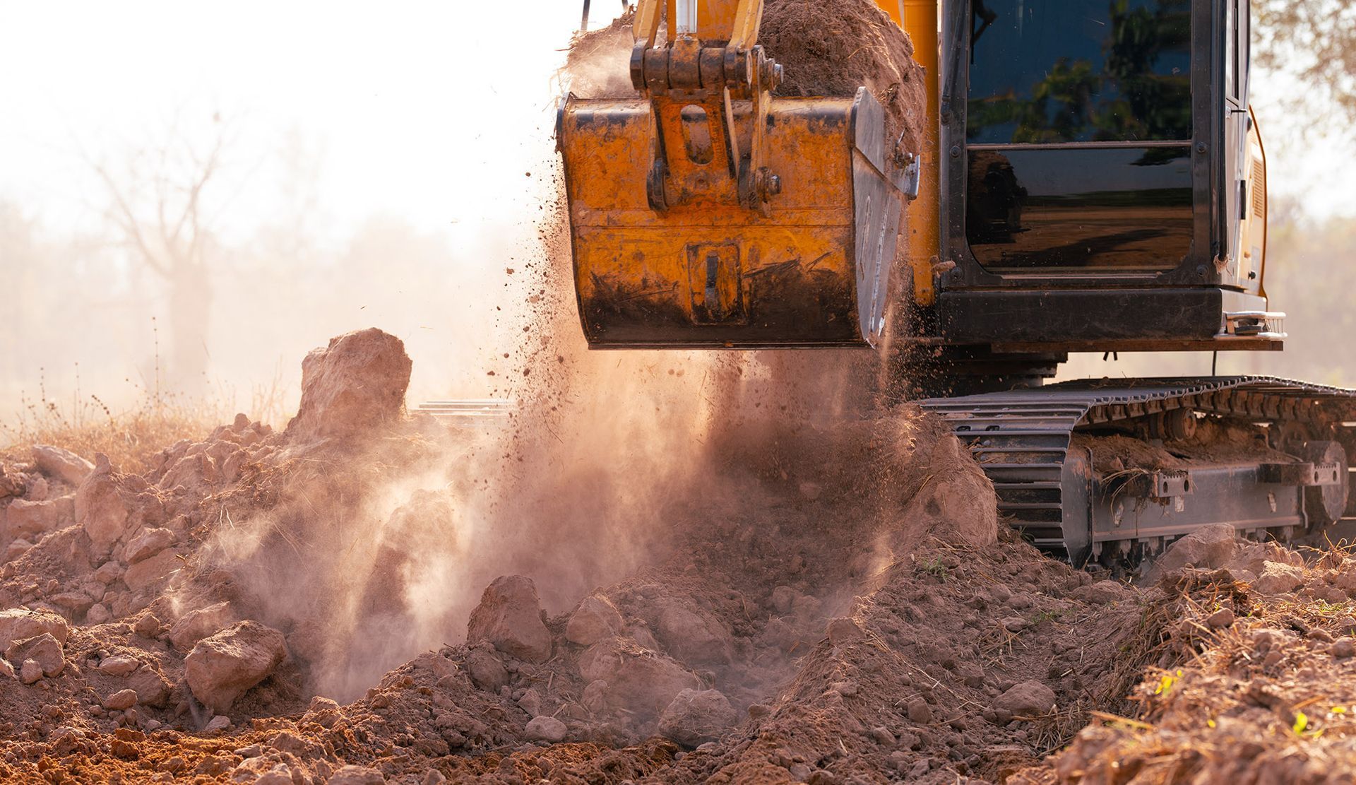 Yellow excavator digging dirt, kicking up dust on a sunny day.