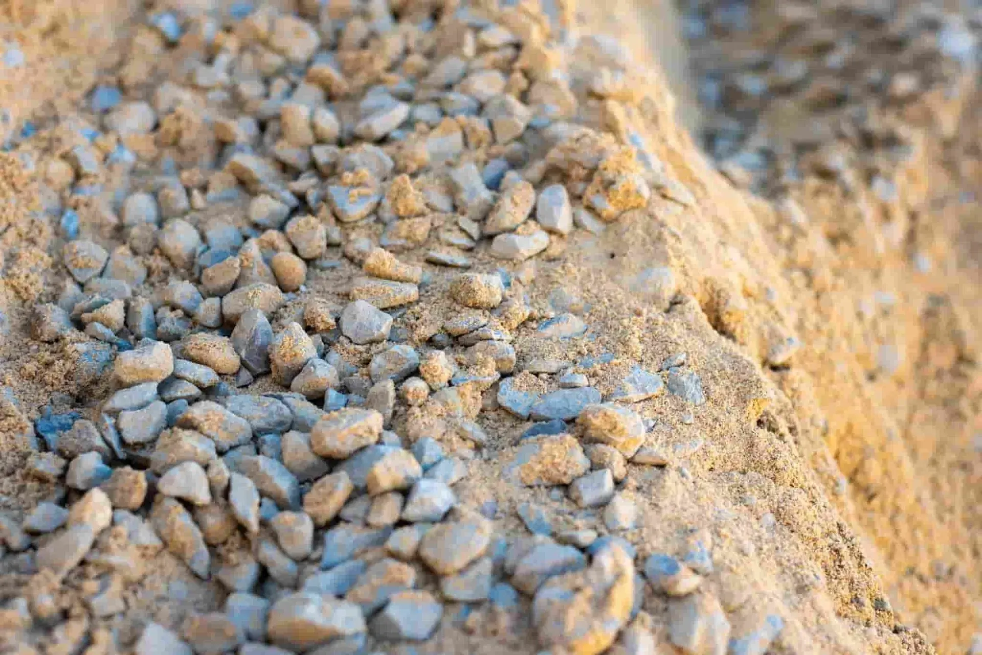 Pile of sand and small gravel, tan and gray tones, close-up shot, sunny outdoor setting.