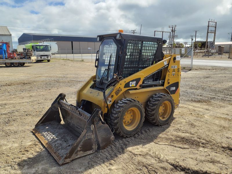 Yellow Caterpillar skid steer loader with bucket on a dirt lot.