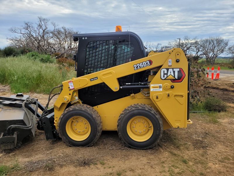 Yellow CAT 279D3 skid-steer loader on dirt, ready for work with dark cab, black attachment, and orange beacon.