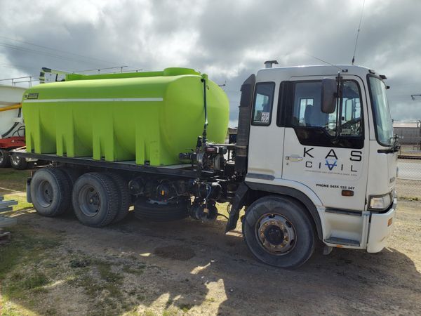 Green water tank on a white KAS Civil truck parked outdoors under a cloudy sky.