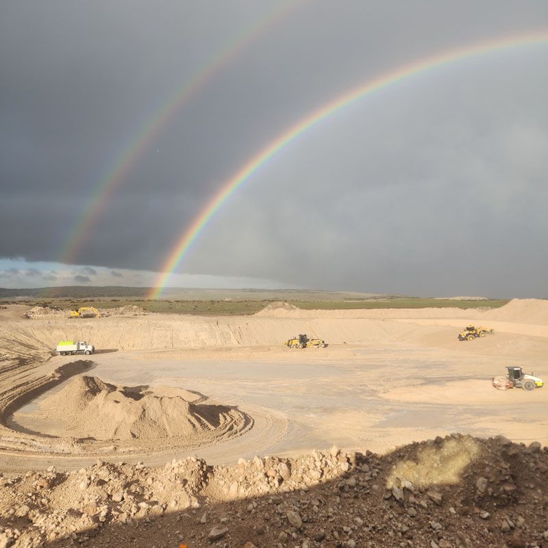 Double rainbow over a construction site with heavy machinery, set against a cloudy sky.