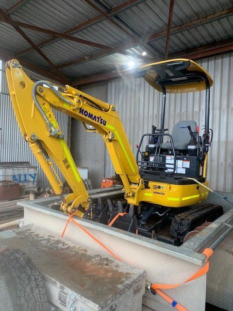 Yellow Komatsu excavator inside a concrete tank, secured with straps. Located inside a warehouse.