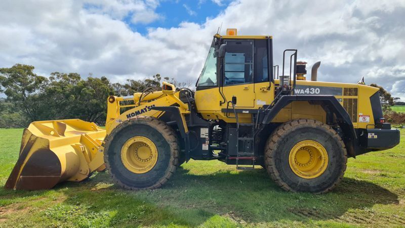 Yellow Komatsu WA430 front-end loader on grass, cloudy sky background.